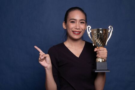 Successful young asian woman holding a trophy on blue backgroundの写真素材