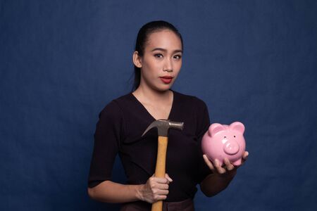 Asian woman with pig coin bank and hammer on blue backgroundの写真素材