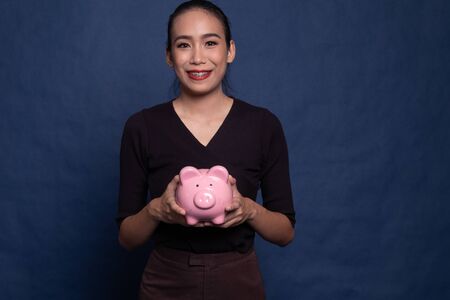 Young Asian woman with a pig coin bank on blue backgroundの写真素材