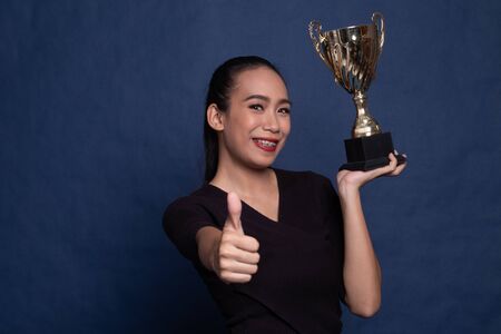 Successful young asian woman holding a trophy on blue backgroundの写真素材