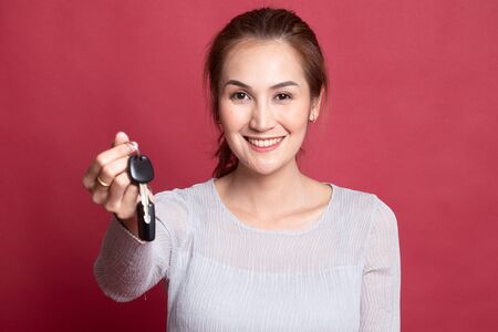 Cute asian girl showing home residence keys on red background