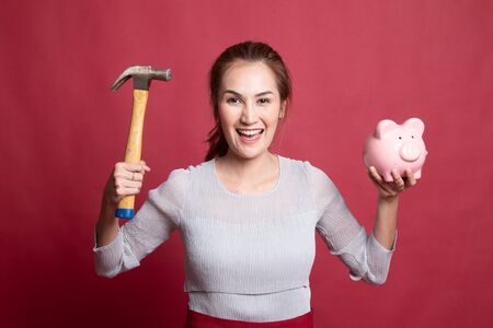 Asian woman with pig coin bank and hammer on red backgroundの写真素材