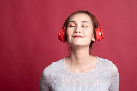 Pretty asian girl listening music with her headphones on red background