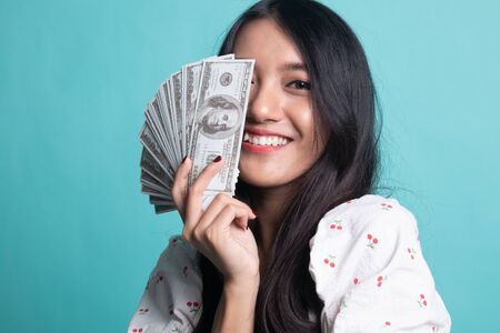 Portrait of  young asian woman  showing bunch of money banknotes on cyan color backgroundの写真素材