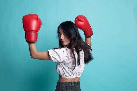 Young Asian woman with red boxing gloves on cyan color backgroundの写真素材