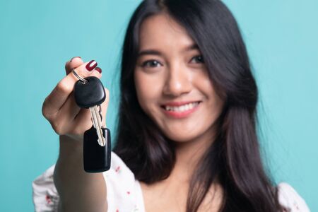 Cute asian girl showing home residence keys on cyan color backgroundの写真素材