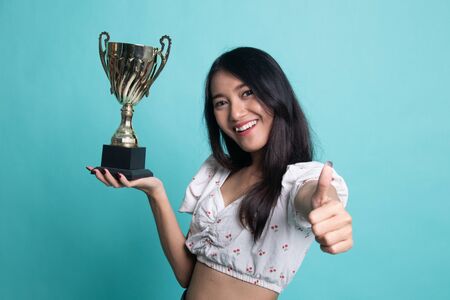 Successful young asian woman holding a trophy show thumb upの写真素材