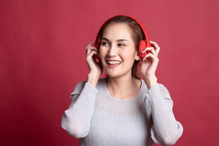 Pretty asian girl listening music with her headphones on red backgroundの写真素材