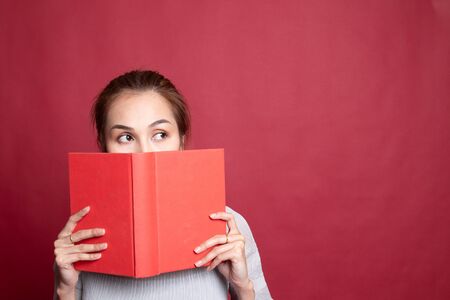 Young Asian woman with a book cover her face on red background