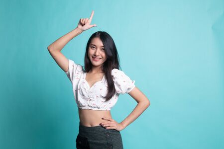 Young Asian woman smile and point up on cyan color background