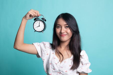Young Asian woman with a clock on cyan color background