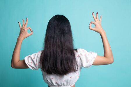 Back view of Asian woman show double OK hand sign on cyan color backgroundの写真素材