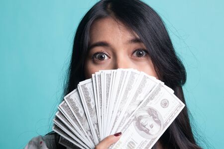 Portrait of  young asian woman  showing bunch of money banknotes on cyan color background