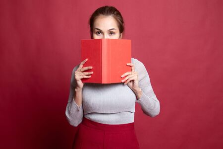 Young Asian woman with a book cover her face on red background