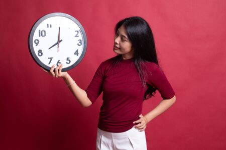 Young Asian woman with a clock on red background.