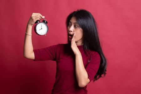 Young Asian woman is stressed with a clock on red background.