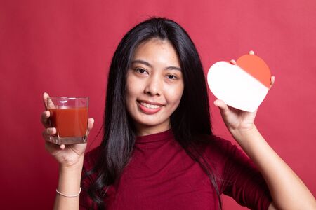 Young Asian woman with tomato juice and red heart on red background.の写真素材