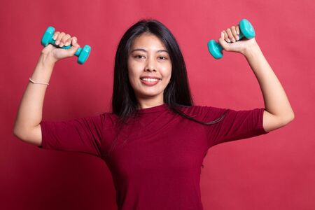 Healthy Asian woman with dumbbells on red background.