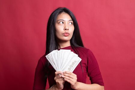 Portrait of  young asian woman  showing bunch of money banknotes on red background.