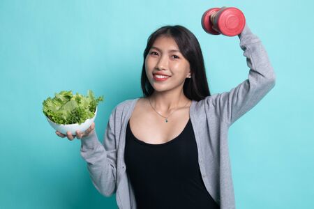 Healthy Asian woman with dumbbells and salad on cyan background.の写真素材