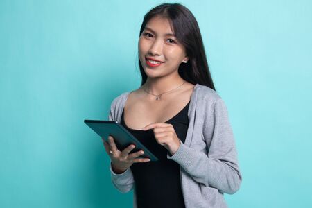 Young Asian woman with a computer tablet on cyan background.の写真素材