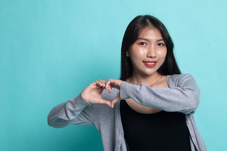 Young Asian woman show heart hand sign on cyan background.の写真素材