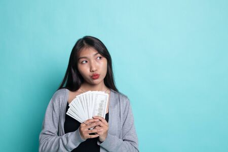 Portrait of  young asian woman  showing bunch of money banknotes on cyan background.の写真素材