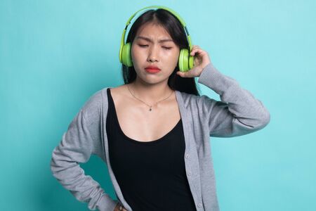 Too loud.  portrait of  young asian woman  holding  headphones and making unhappy face on cyan background.の写真素材