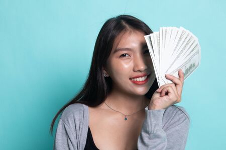 Portrait of  young asian woman  showing bunch of money banknotes on cyan background.の写真素材