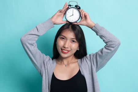 Young Asian woman smile with a clock on cyan background.の写真素材