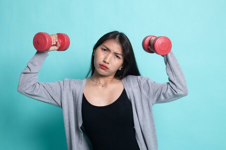 Exhausted Asian woman with dumbbells on cyan background.の写真素材