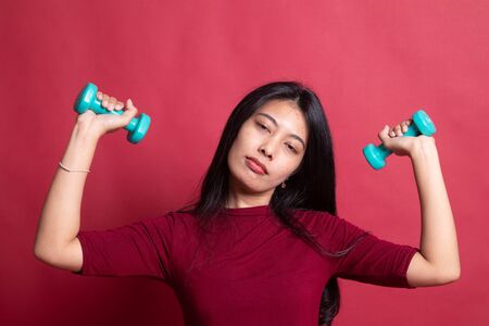 Exhausted Asian woman with dumbbells on red background.の写真素材
