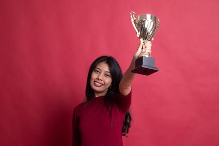 Successful young asian woman holding a trophy on red background.の写真素材