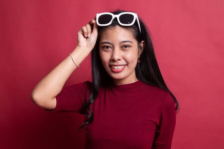 Portrait of a beautiful young asian girl in sunglasses on red background.の写真素材
