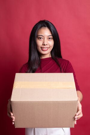 Delivery, relocation and unpacking.  young asian woman holding cardboard box on red background.