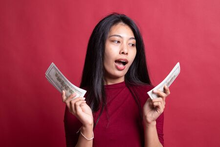 Portrait of  young asian woman  showing bunch of money banknotes on red background.の写真素材