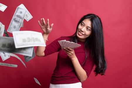 Portrait of very happy  young asian woman throwing out money banknotes on red background.