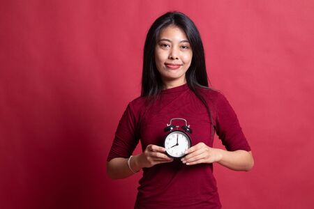 Young Asian woman smile with a clock on red background.の写真素材