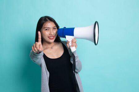 Beautiful young Asian woman announce with megaphone on cyan background.