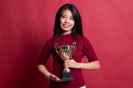 Successful young asian woman holding a trophy on red background.の写真素材