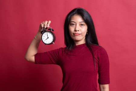 Young Asian woman with a clock on red background.の写真素材