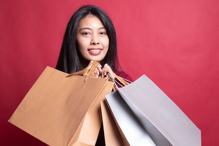 Beautiful young Asian woman with shopping bags on red background.の写真素材