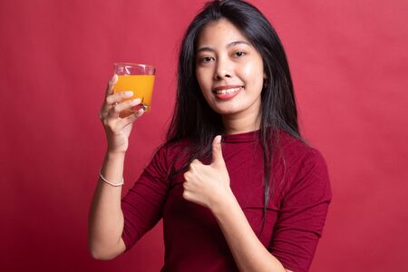 Young Asian woman thumbs up drink orange juice on red background.の写真素材