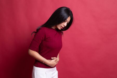 Young Asian woman got stomach ache on red background.の写真素材