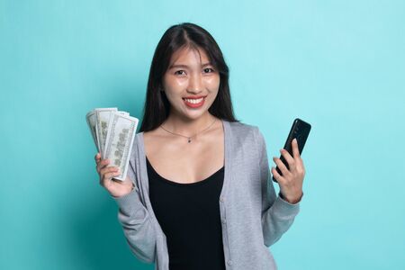 Portrait of  young asian woman  showing bunch of money banknotes on cyan background.の写真素材
