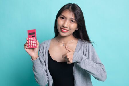 Asian woman thumbs up with calculator on cyan background.の写真素材