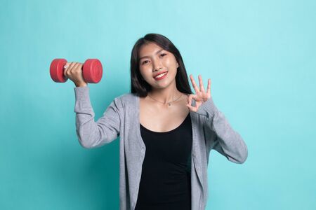 Healthy Asian woman show OK with dumbbells on cyan background.の写真素材