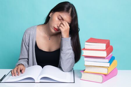 Exhausted Asian woman got headache read a book with books on table on cyan background.の写真素材