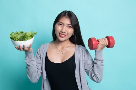 Healthy Asian woman with dumbbells and salad on cyan background.の写真素材