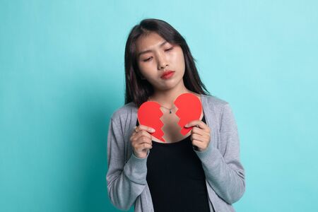 Beautiful young Asian woman with broken heart on cyan background.の写真素材